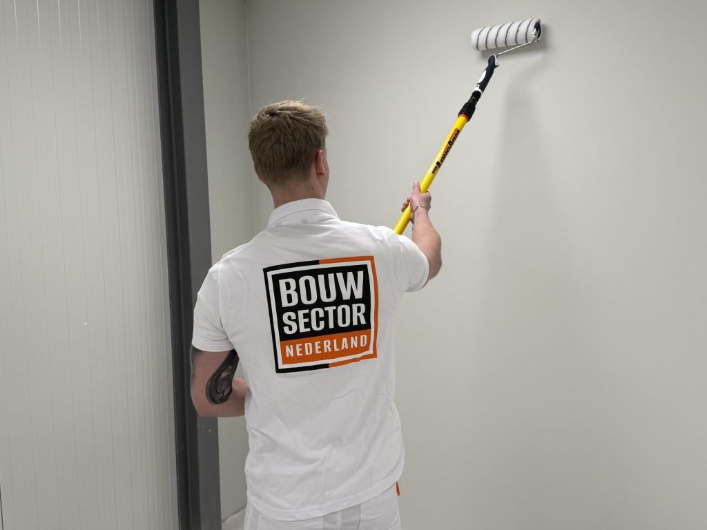 Schilder in wit poloshirt zet een lichte wand in de verf met een roller aan een verlengsteel