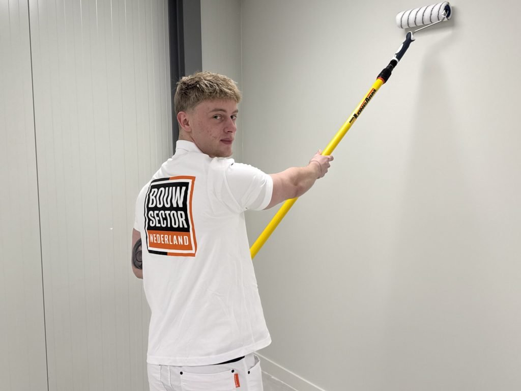 Schilder van Bouwsector Nederland kijkt om terwijl hij een lichte muur met een lange roller saust